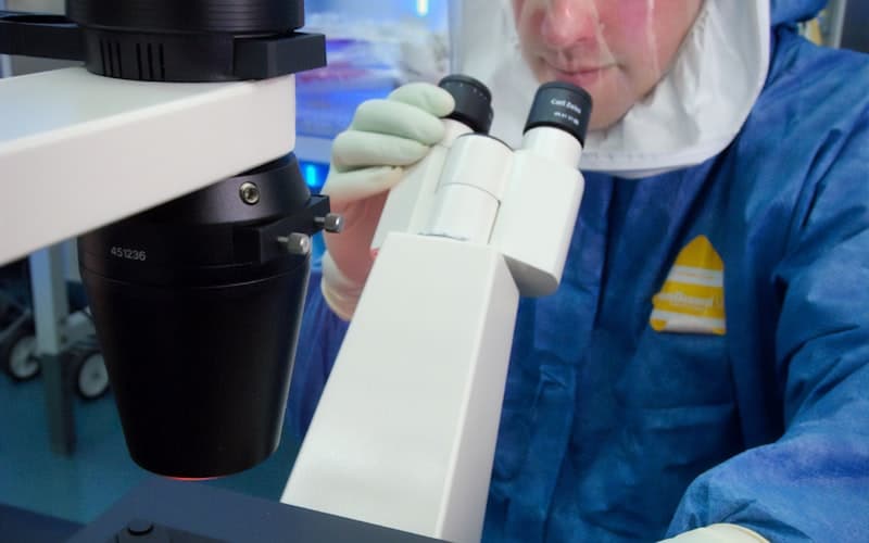 Scientist examining samples through a microscope in a pharma lab